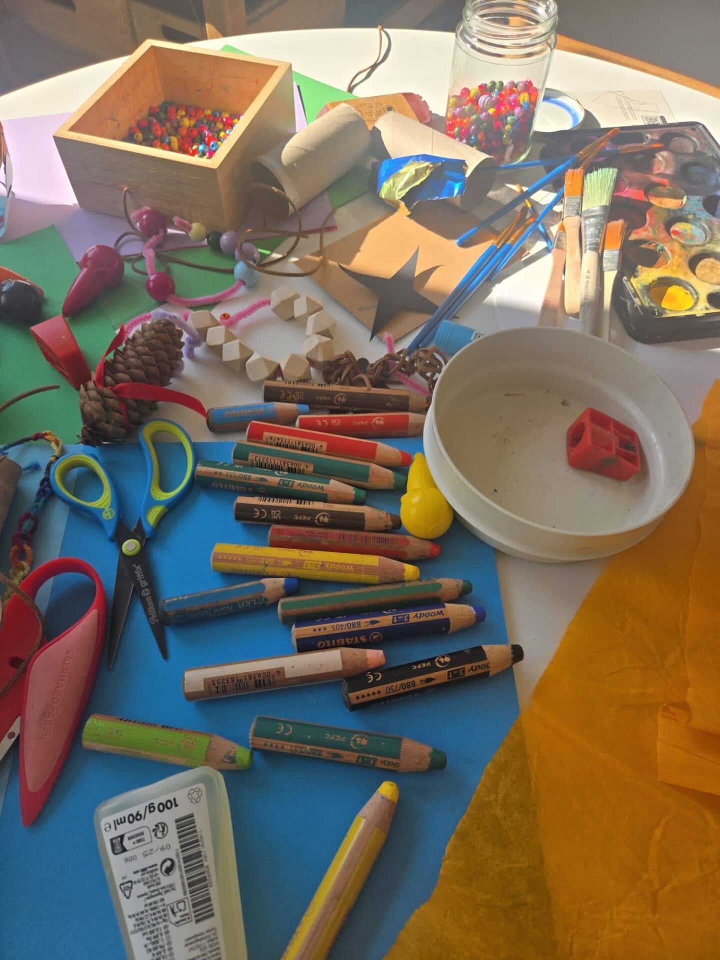 Auf einem Tisch liegen Bastelutensilien: Schere, Stifte, buntes Papier uvm.