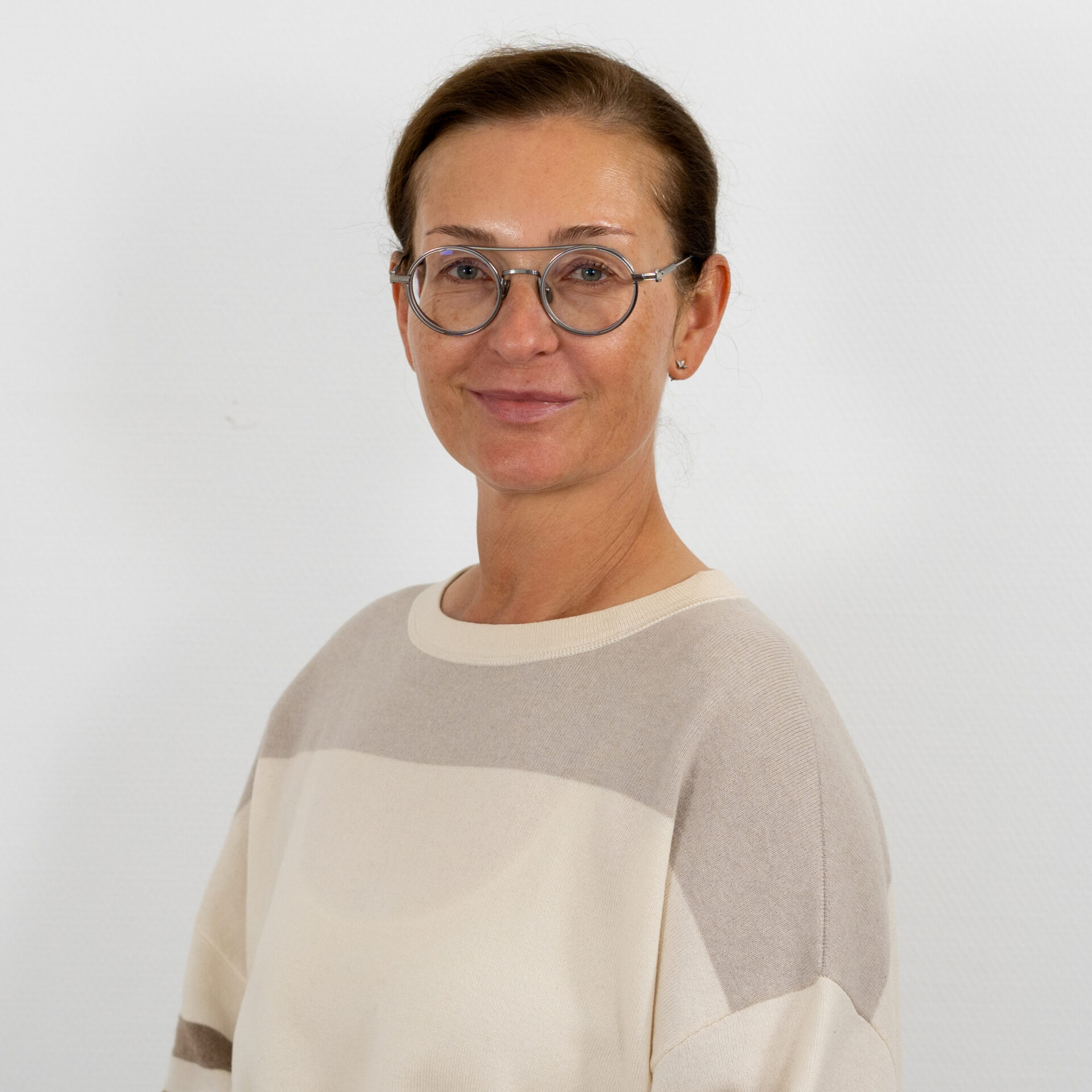 Eine Person mit Brille und zurückgekämmten Haaren, die einen hellen Pullover trägt, posiert vor einem schlichten weißen Hintergrund.