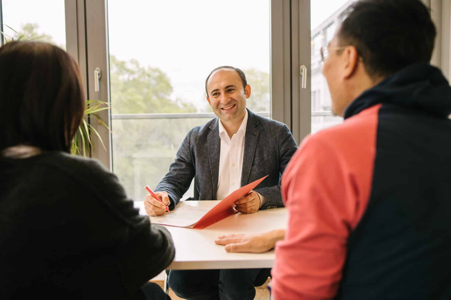 Ein Mann sitzt am Tisch und berät zwei Personen.