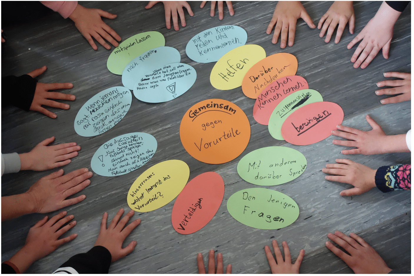 Bunte Karten mit Strategien gegen Vorurteile liegen auf einem Tisch. Um die Karten sind Kinderhände zu sehen.