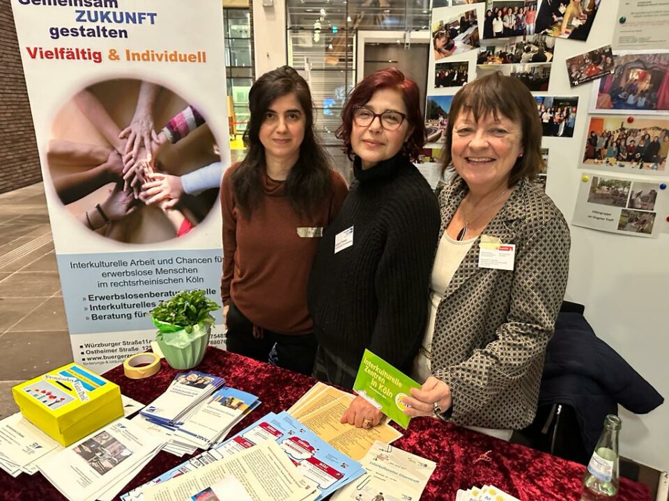 Drei Frauen verteilen Flyer an einem Stand beim Tag der Muttersprache.