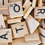 Ein Stapel verstreuter hölzerner Scrabble-Spielsteine mit schwarzen Buchstaben und Zahlen.