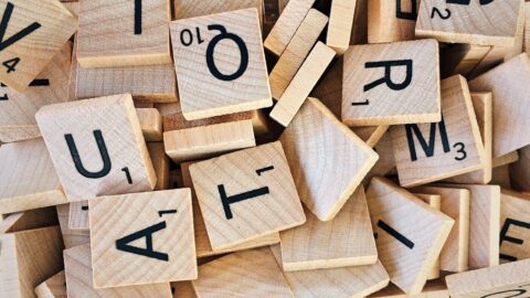 Ein Stapel verstreuter hölzerner Scrabble-Spielsteine mit schwarzen Buchstaben und Zahlen.